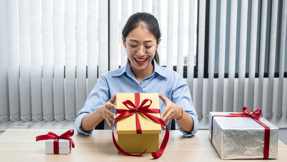 ผู้หญิงวัยทำงานเปิดกล่องของขวัญจากเพื่อนร่วมงาน